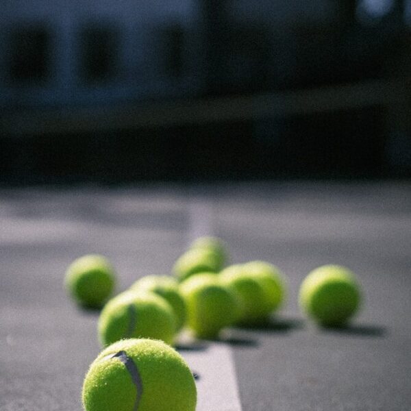 Close-up vergelijking tussen een gele padelbal en tennisbal op een padelbaan – Padelballen vs tennisballen verschil.