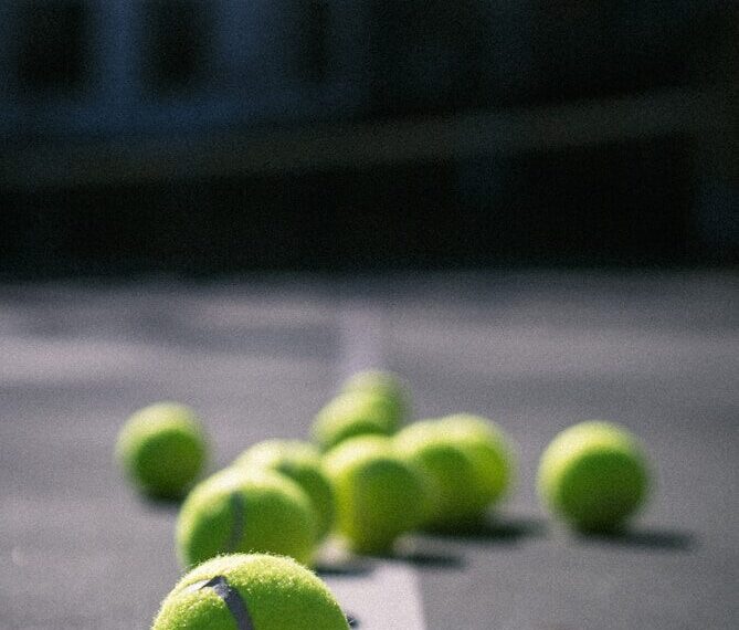 Close-up vergelijking tussen een gele padelbal en tennisbal op een padelbaan – Padelballen vs tennisballen verschil.