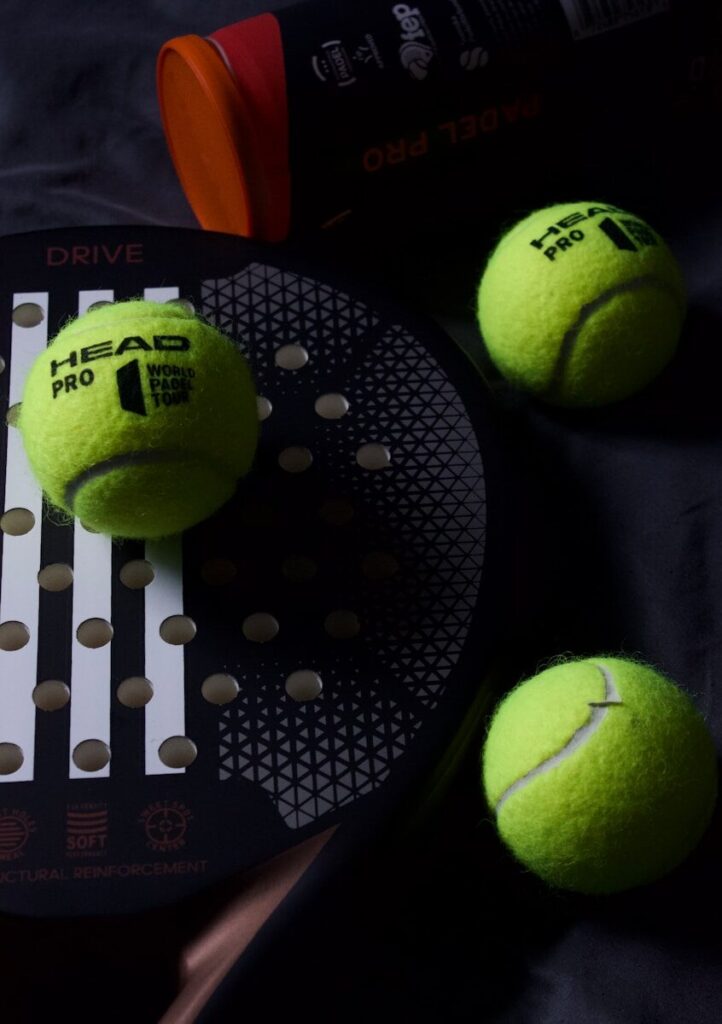 three tennis balls and a racket on a bed